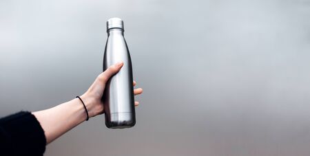 Close-up of female hand holding reusable, steel thermo shiny bottle for water. Copy space concept.の写真素材