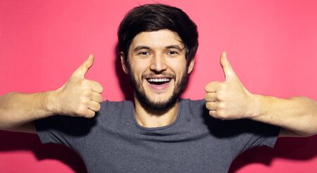 Portrait of young happy man show thumbs up, isolated on coral pink background.