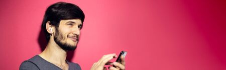 Portrait of young confident man using wireless earphones and smartphone. Copy space concept on...