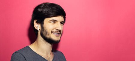 Portrait of smiling man with wireless earphones on background of pink coral.