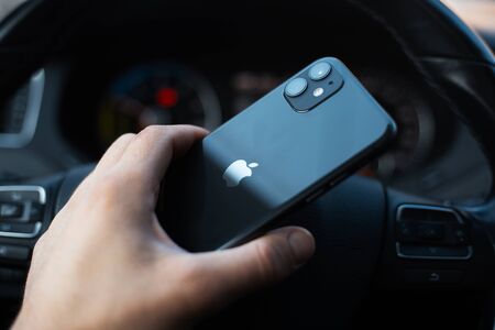 Chisinau, Moldova - 03.12.2019: Close-up of male hand, holding a iPhone 11 on background of steering wheel of car.のeditorial素材
