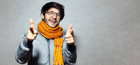 Portrait of happy man pointing fingers on camera, wearing glasses and orange scarf with grey bomber.の写真素材