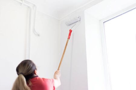 Portrait of woman who paint wall in apartment with white color and roller.の写真素材