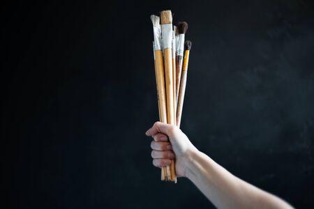 Close-up of female holding a lot of brushes on black background.