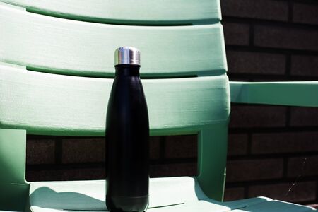 Close-up of reusable thermo water bottle on green chair.