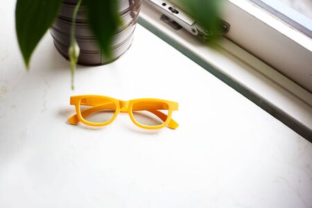 Close-up of yellow glasses on window sill near plant.の写真素材