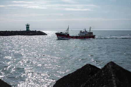 View from afar of nave ship on the sea, on the background of blue sky and a lighthouse.
