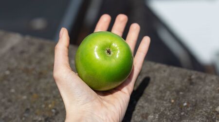 Close-up of female hand holding green apple outdoors.の写真素材