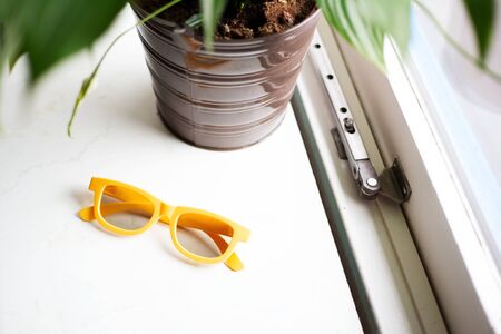 Close-up of yellow glasses on window sill near plant.の写真素材