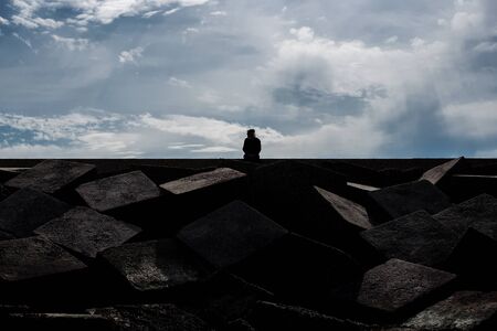 Silhouette of man sitting on top of square stones against the sky background.の写真素材