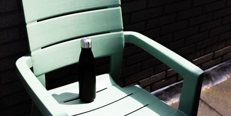 Close-up of reusable thermo water bottle on green chair.