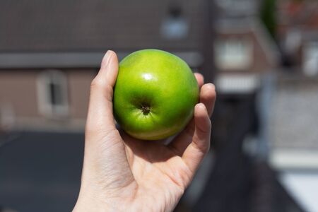 Close-up of female hand holding green apple outdoors.の写真素材