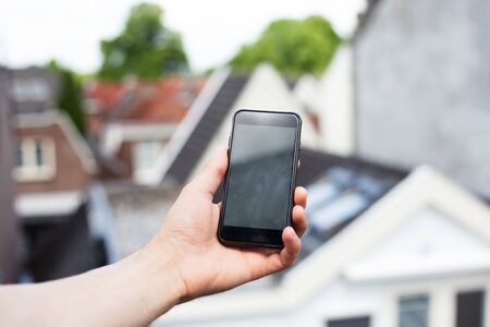 Close-up of male hand hold smartphone on background of old city.