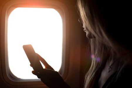 Arm of girl holding the smartphone on background of airplane window.の写真素材