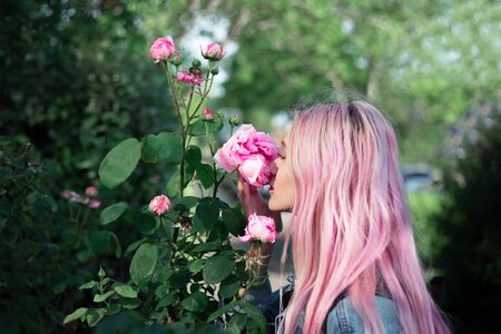 Portrait of young girl with pink hair sniffing rose flower.の写真素材