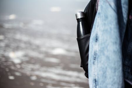 Steel reusable water bottle in the pocket of backpack on the background of sea shore.の写真素材