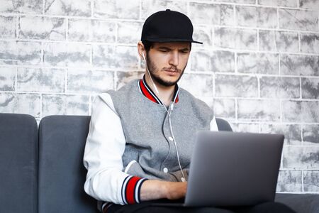 Portrait of young freelancer guy, sitting on sofa with cup of coffee in hand and laptop on legs....