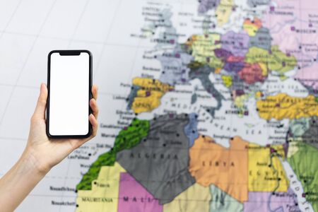Close-up of female hand holding smartphone with mockup on background of Europe map.の写真素材