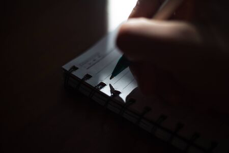 Close-up of male hand writing in notebook with pen.