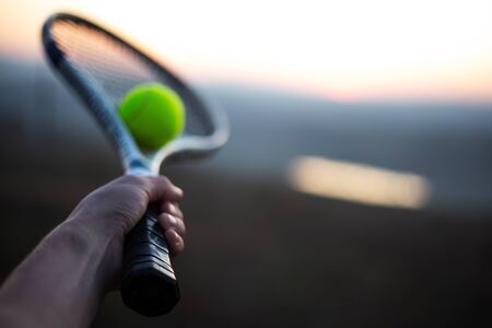Close-up of male hand holding tennis racket with ball outdoors.の写真素材