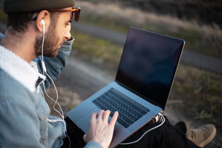 Portrait of young hipster man using laptop outdoor.