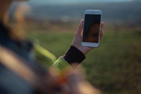 Close-up of female hand holding smartphone on background of sunset.の写真素材