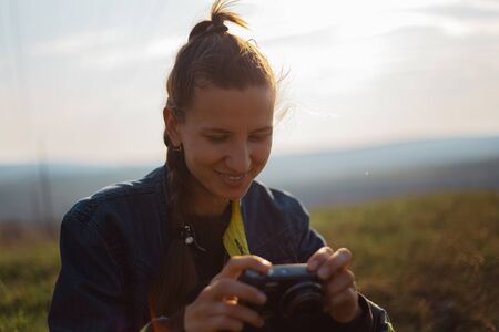Portrait of young girl holding digital photo camera on background of sunset.