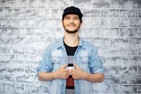 Portrait of young man in blue denim jacket, on the background of grey brick wall.