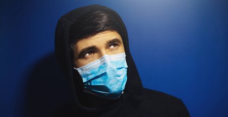 Close-up portrait of man looking up, wearing medical protective flu mask and hooded sweatshirt, on background of yellow color with copy space.の写真素材