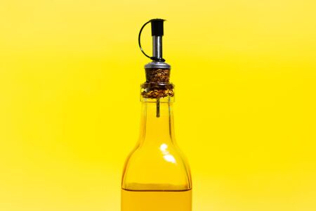 Close-up of glass bottle with olive oil, closed with special cap, isolated on yellow background.の写真素材