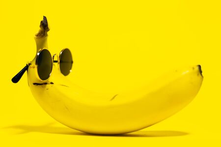 Close-up of yellow banana wearing round sunglasses lying on background of yellow color.の写真素材