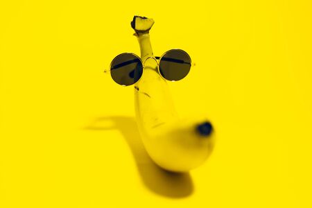 Close-up of yellow banana wearing round sunglasses lying on background of yellow color.の写真素材