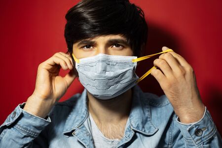 Studio portrait of young sick guy in denim jacket, put on medical face mask against coronavirus,...