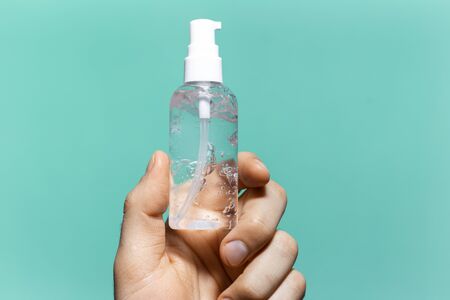 Close-up of male hand holding small plastic bottle of sanitizer antibacterial gel on background of...
