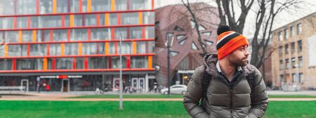 Panoramic banner portrait of young guy with orange hat on background of spring modern city.の写真素材