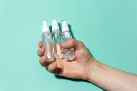 Close-up of male hand holding portable plastic dispenser bottles with sanitizer antiseptic,...