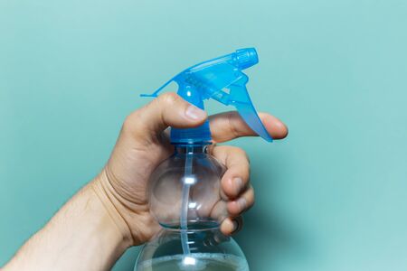 Close-up of male hand holding spray bottle for cleaning with blue pump, on cyan background.の写真素材