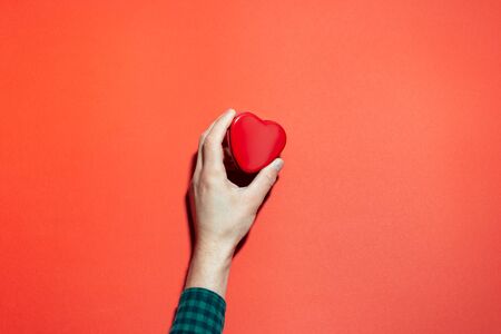 Close-up of male hand holding shape of red heart on background of red color.の写真素材