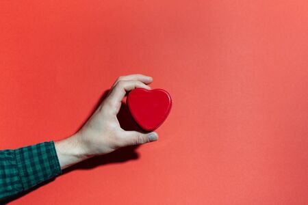 Close-up of male hand holding shape of red heart on background of red color.の写真素材