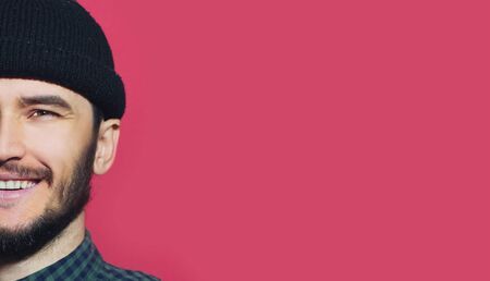 Half face portrait of young smiling hipster man wearing beanie hat on background of pastel pink with copy space.の写真素材
