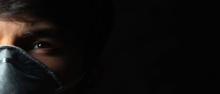 Coronavirus prevention. Close-up portrait of young guy wearing protective medical respiratory mask against flu, on black background. Macro photo.の写真素材