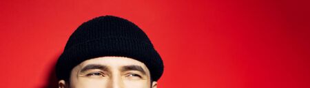 Close-up of smiling eyes of asian guy wearing black beanie hat, panoramic portrait on red background.の写真素材