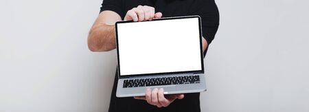 Close-up of male hands holding opened laptop with mockup on screen, panoramic banner background of...