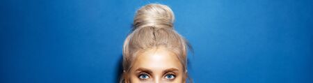 Panoramic portrait of woman head with blue eyes, blonde hair wrapped in a bun, on background of phantom blue color.の写真素材