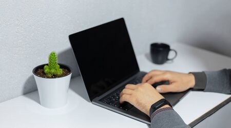 Close-up of businessman hands typing on laptop keyboard, wearing smartwatch, coffee cup and cactus...