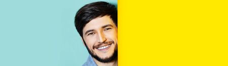 Studio portrait of young smiling guy between two backgrounds of yellow and aqua menthe colors.の写真素材