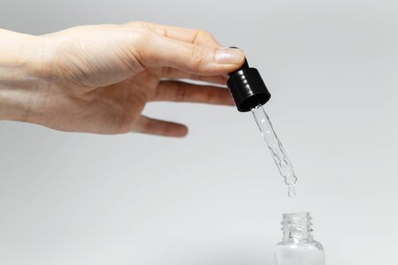 Close-up of female hand holding pipette of essential skin care oil, drops in small glass bottle. Studio background of white.の写真素材