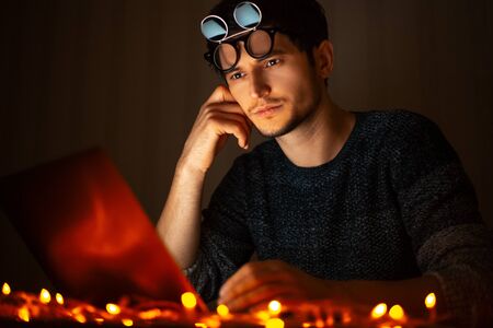 Portrait of young guy wearing shades, working at laptop in dark room home, pc beside garlands.の写真素材