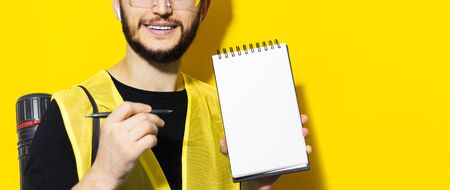 Studio portrait of young smiling engineer man showing with pen on empty notebook with mockup. Using...
