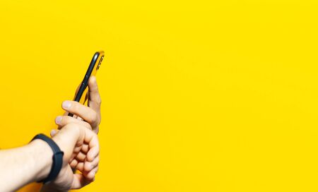Close-up of male hands, holding and using modern smartphone and smartwatch, verifies time. Studio background of yellow color with copy space.の写真素材